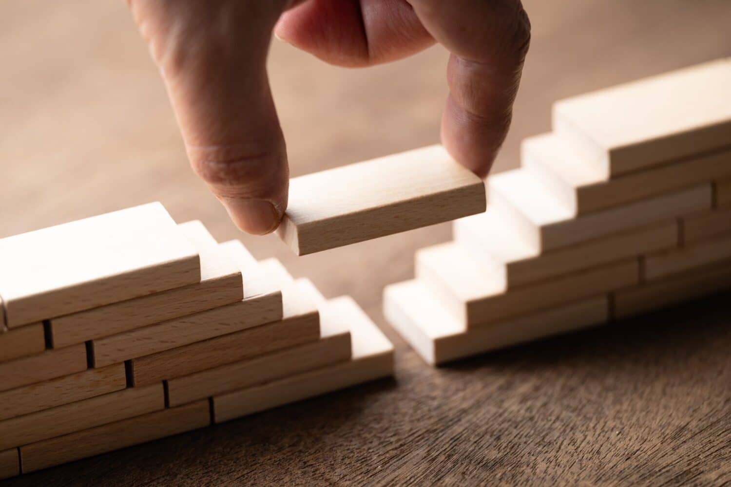 A hand places a wood block to connect two separate piles of blocks. Metaphorically 'Bridging the Gap between Accounting and Operations'