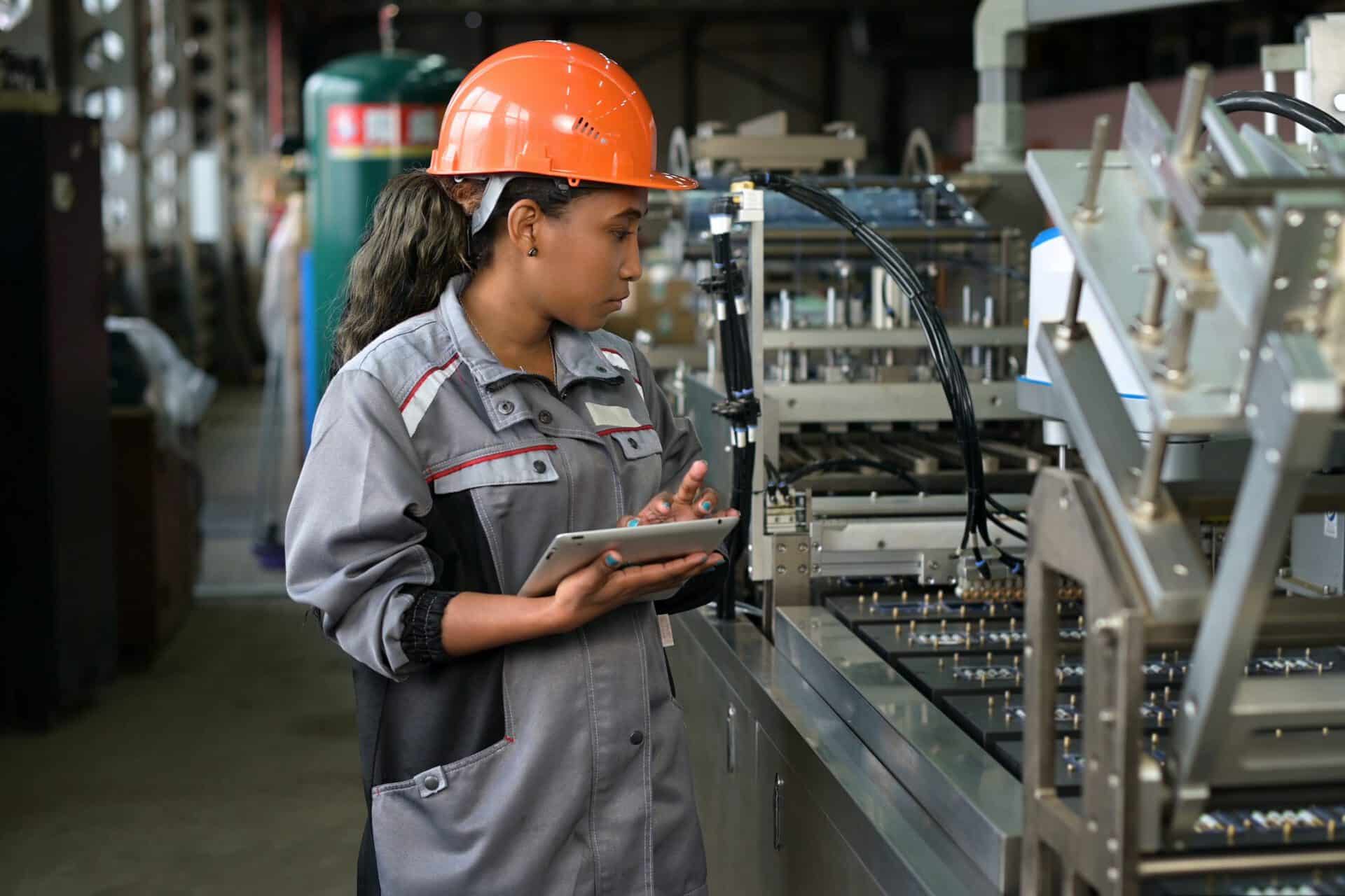Women in hard hat with tablet monitoring assembly line