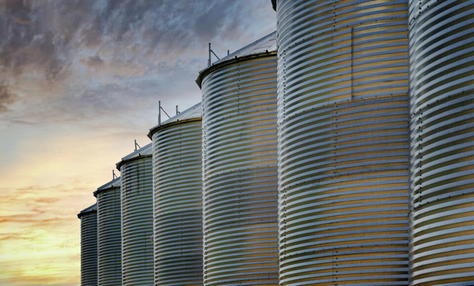 Row of grain silos silhouetted against a sunset