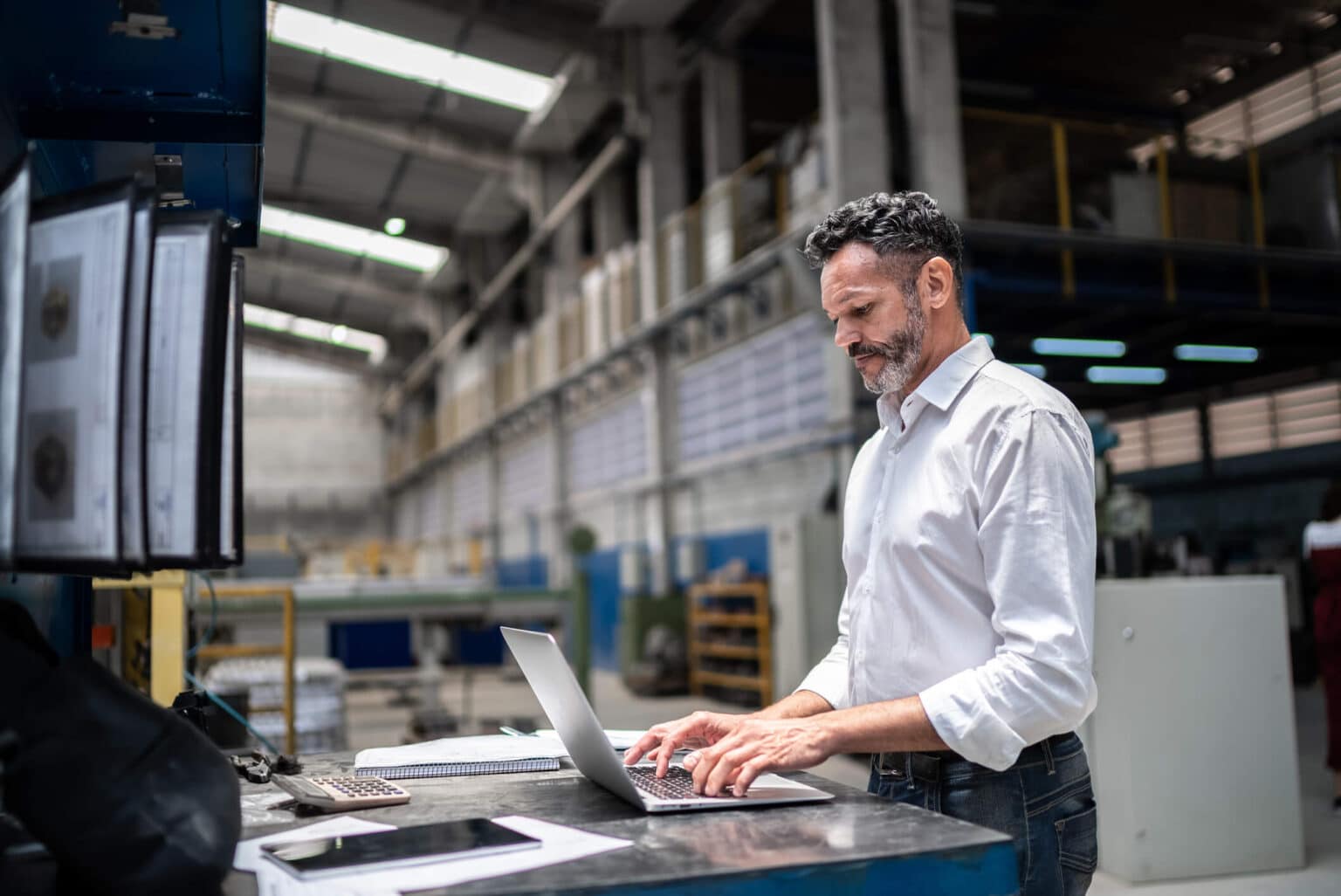 Man working on laptop standing in warehouse.