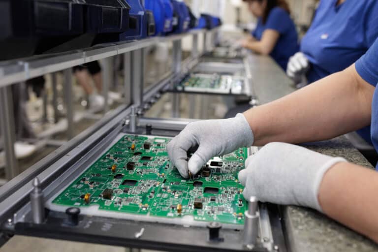 Techniker mit Handschuhen bei der Bestückung einer Leiterplatte an einer modernen SMT-Fertigungslinie